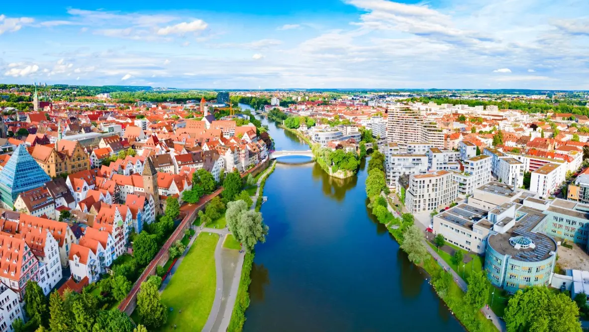 A stone arch bridge spans a calm river, flanked by classic red-roofed buildings, offering a peaceful and picturesque journey into history on a cruise.