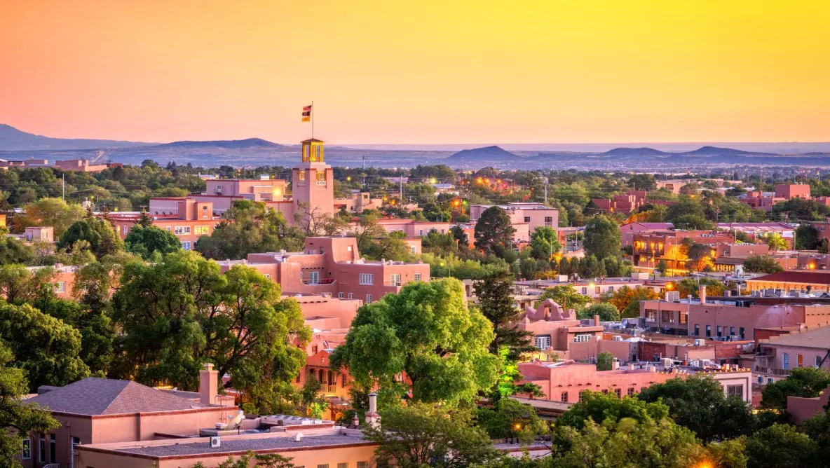 A historic Mexican town with a flag-topped tower against golden sunset mountains, reflecting the rich culture and scenic beauty of cruise destinations