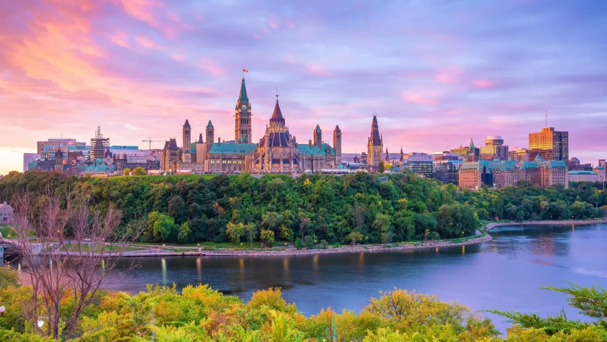 A historic castle beneath a purple sunset sky, surrounded by trees and a clear river, reflecting the storybook charm of New England and Canada routes.