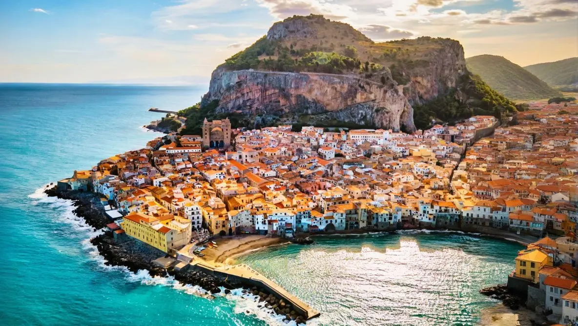 A historic Mediterranean town nestled between a calm blue sea and rolling mountains, offering timeless coastal charm and a peaceful atmosphere.