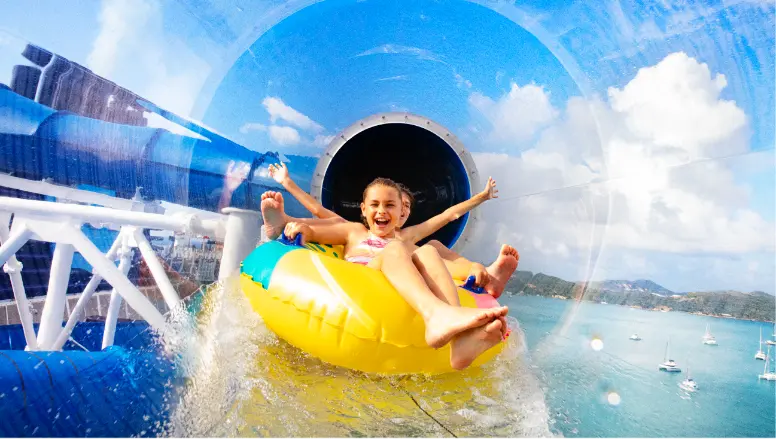 A wide shot of the expansive Aqua Park on a Norwegian Cruise Line ship, showcasing bright blue and yellow water slides under a sunny sky.