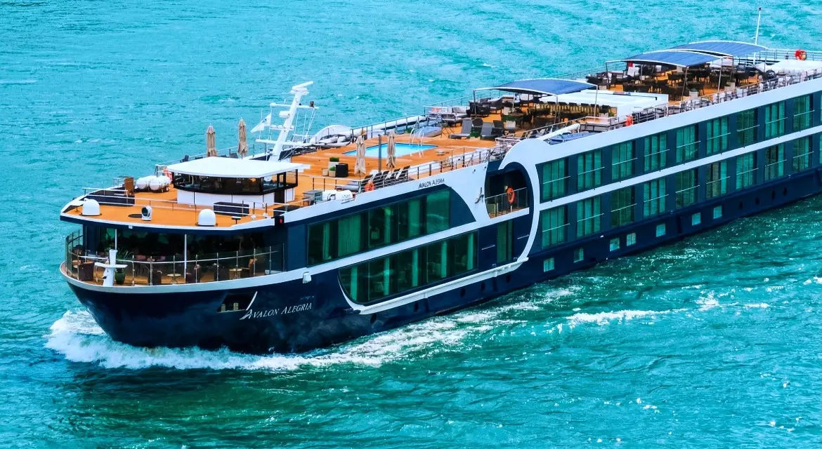 Avalon Waterways 2026 cruise collection: signature Suite Ship with a majestic mountain backdrop, showcasing Panorama Suites. An Avalon Suite Ship sails past dramatic peaks, showcasing 2026 Active & Discovery cruises through Europe’s most scenic waterways.