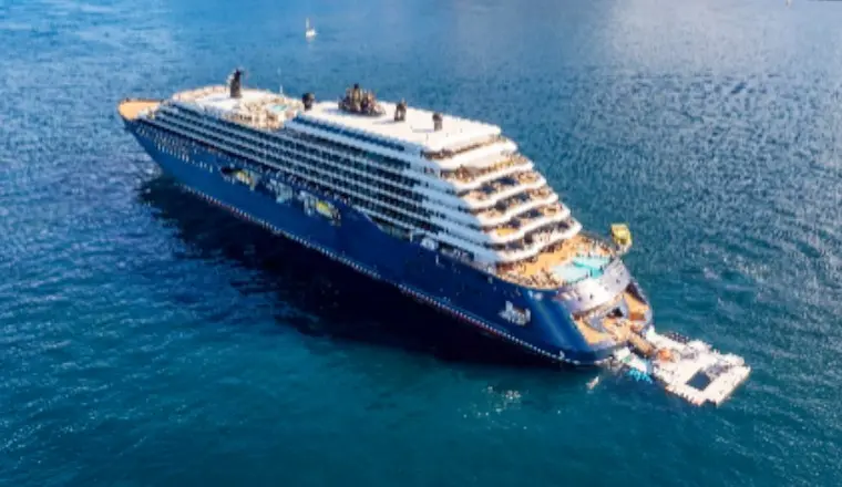 A luxury Ritz-Carlton yacht cruises through a tropical bay. Golden side-lighting highlights its sleek white hull against shimmering turquoise sea.