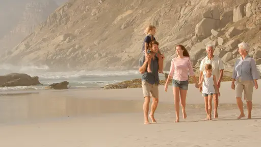 Tres generaciones caminando felices por la orilla del mar, disfrutando juntos de un momento familiar alegre y relajante.
