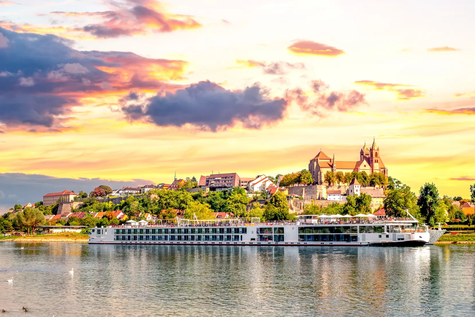 Un crucero por el río navegando por un río al atardecer con un castillo europeo al fondo.