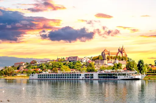 Un crucero por el río navegando por un río al atardecer con un castillo europeo al fondo.