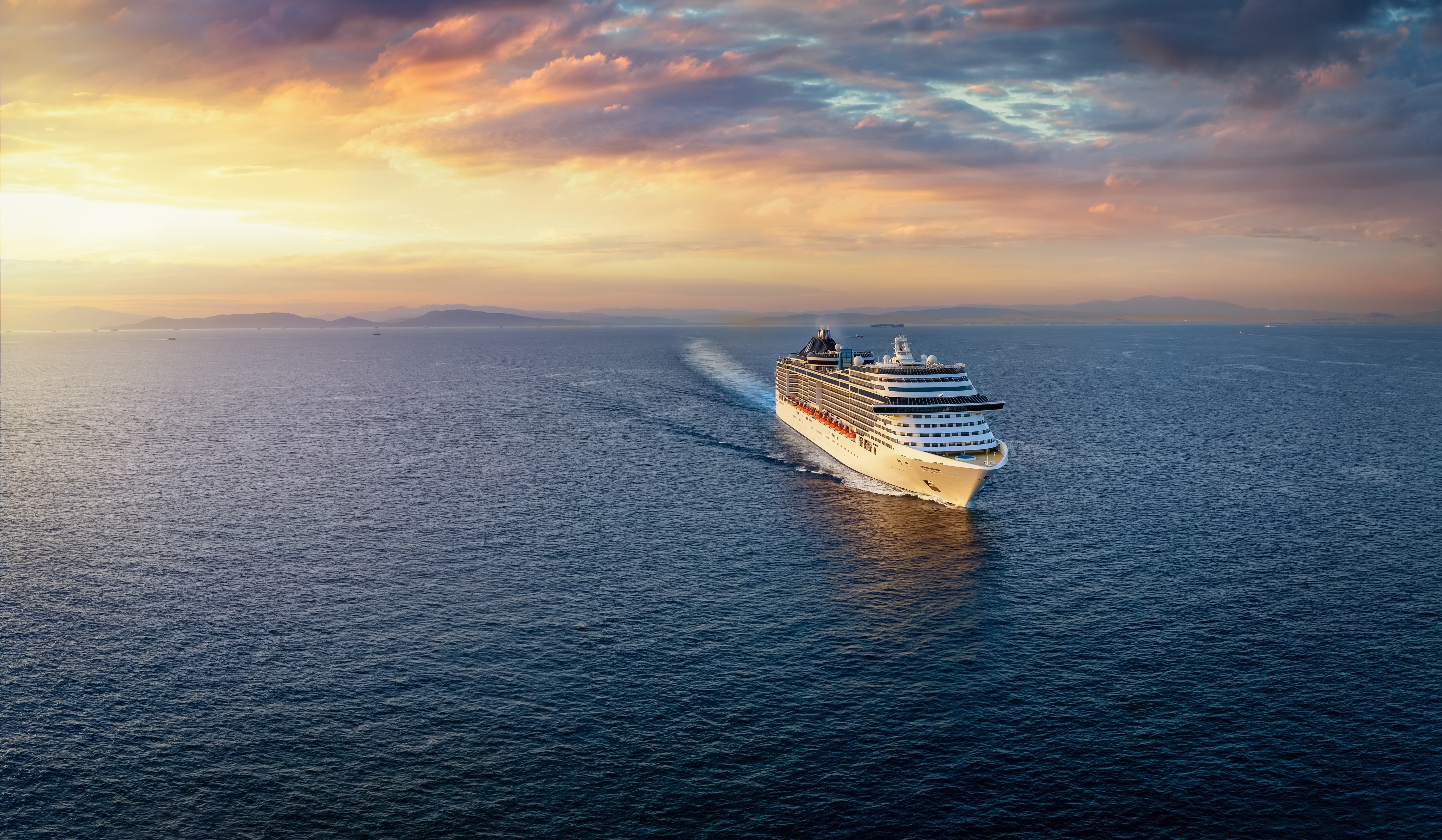 A cruise ship traveling over the ocean during golden summer sunset time