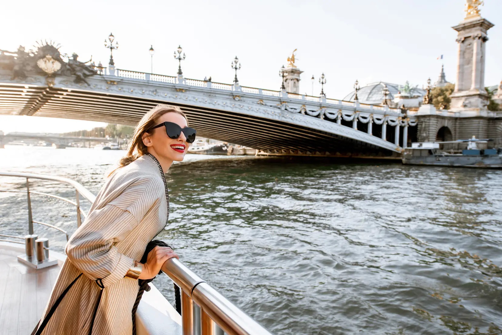 Una mujer con gafas de sol se encuentra en la cubierta de un crucero por el río cuando se acerca a un puente.