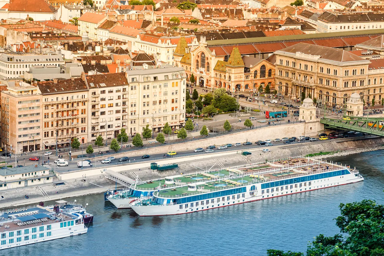 Varios cruceros fluviales atracaron en un puerto con edificios de ciudades europeas al fondo.