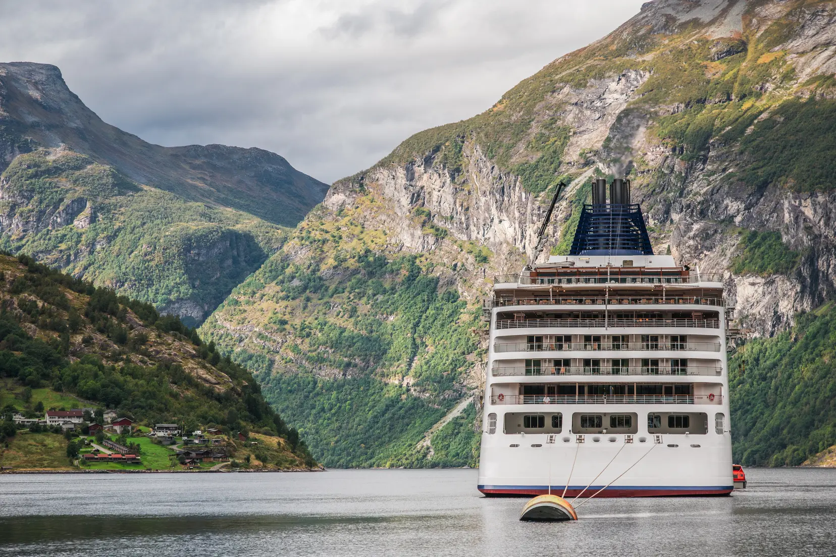 A large cruise ship docked at Geirangerfjord in Norway, anchored at the port of Geiranger, surrounded by mountains on all sides