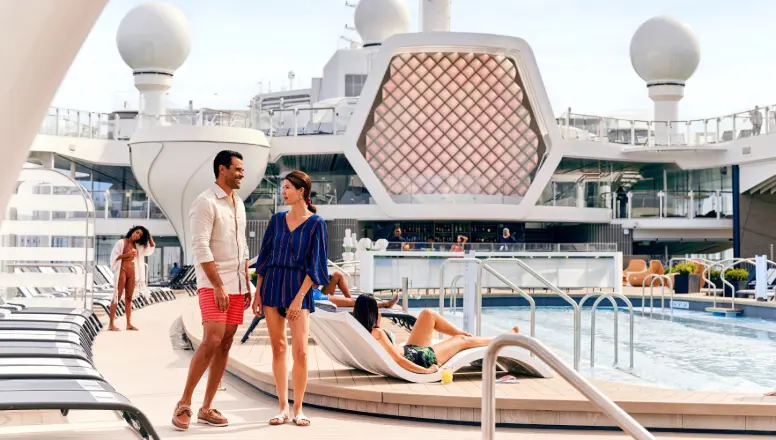 Pareja disfrutando de la terraza de la piscina en un barco de Celebrity Cruises, con tumbonas, una espectacular piscina y la arquitectura moderna característica del barco.