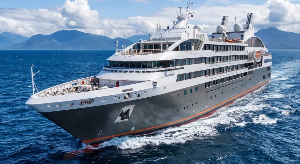 A Ponant expedition yacht cuts through calm coastal waters beneath dramatic mountain peaks, capturing the line's blend of luxury and remote exploratio