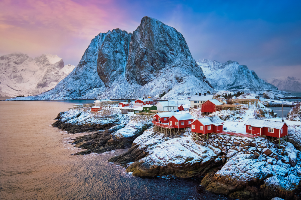 The famous Hamnøy fishing village in Norway's Lofoten Islands, renowned for its iconic red rorbu cabins, blanketed in snow during a winter sunrise.