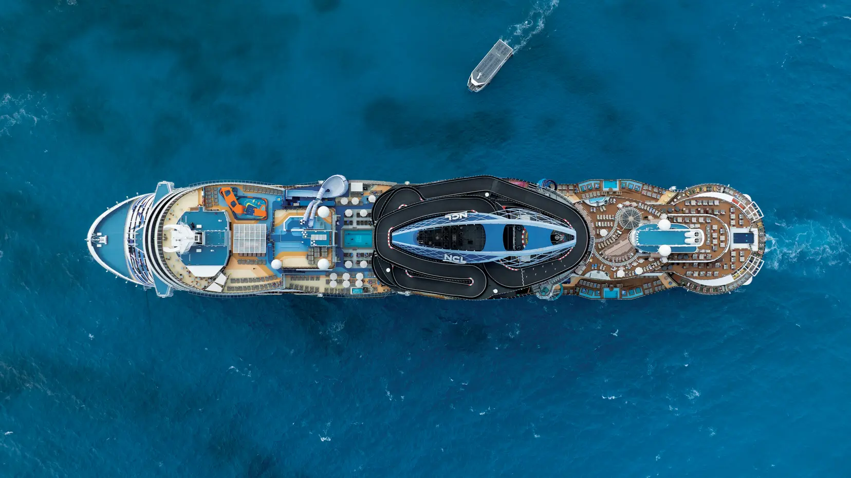 Aerial view of NCL's cruise ship sailing the open ocean, featuring colorful water slides, pools, and expansive deck amenities