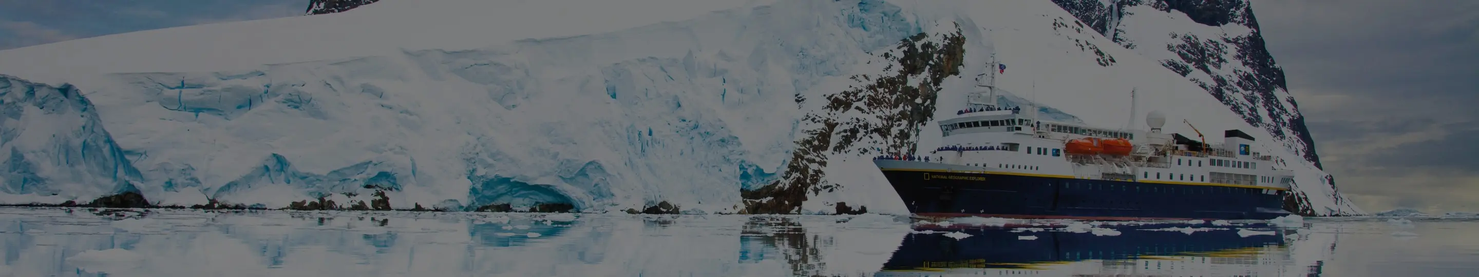 The National Geographic Explorer glides past towering glaciers and icebergs in Antarctica, showcasing the intimate scale of Lindblad Expeditions.