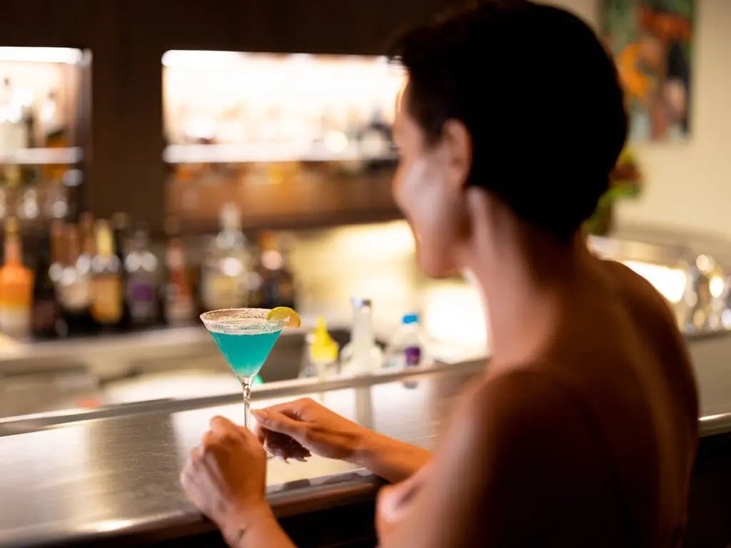 A guest enjoys a signature blue cocktail at the onboard bar aboard the m/s Paul Gauguin, capturing the relaxed, all-inclusive lounge atmosphere at sea