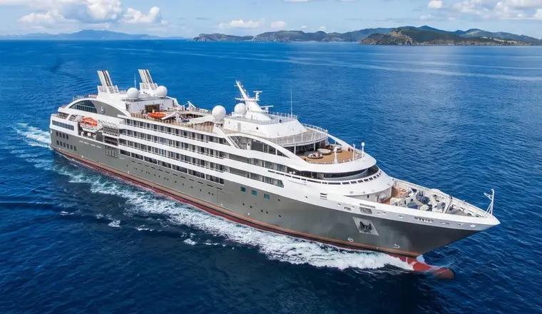A Ponant megayacht cruises past a chain of green tropical islands, showcasing the sleek design and small-ship access that define the fleet.
